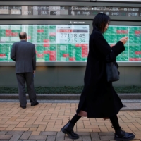 A woman walks past a man examining an electronic board showing the 225-issue Nikkei average and stock quotations outside a brokerage in Tokyo on Monday. | REUTERS