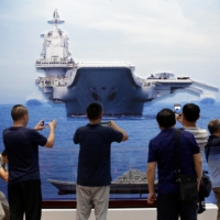 Visitors take photos of exhibits showing the Chinese People\'s Liberation Army Navy\'s first aircraft carrier, the Liaoning, during an exhibition at the Beijing Exhibition Center in the Chinese capital in September, 2019. | REUTERS