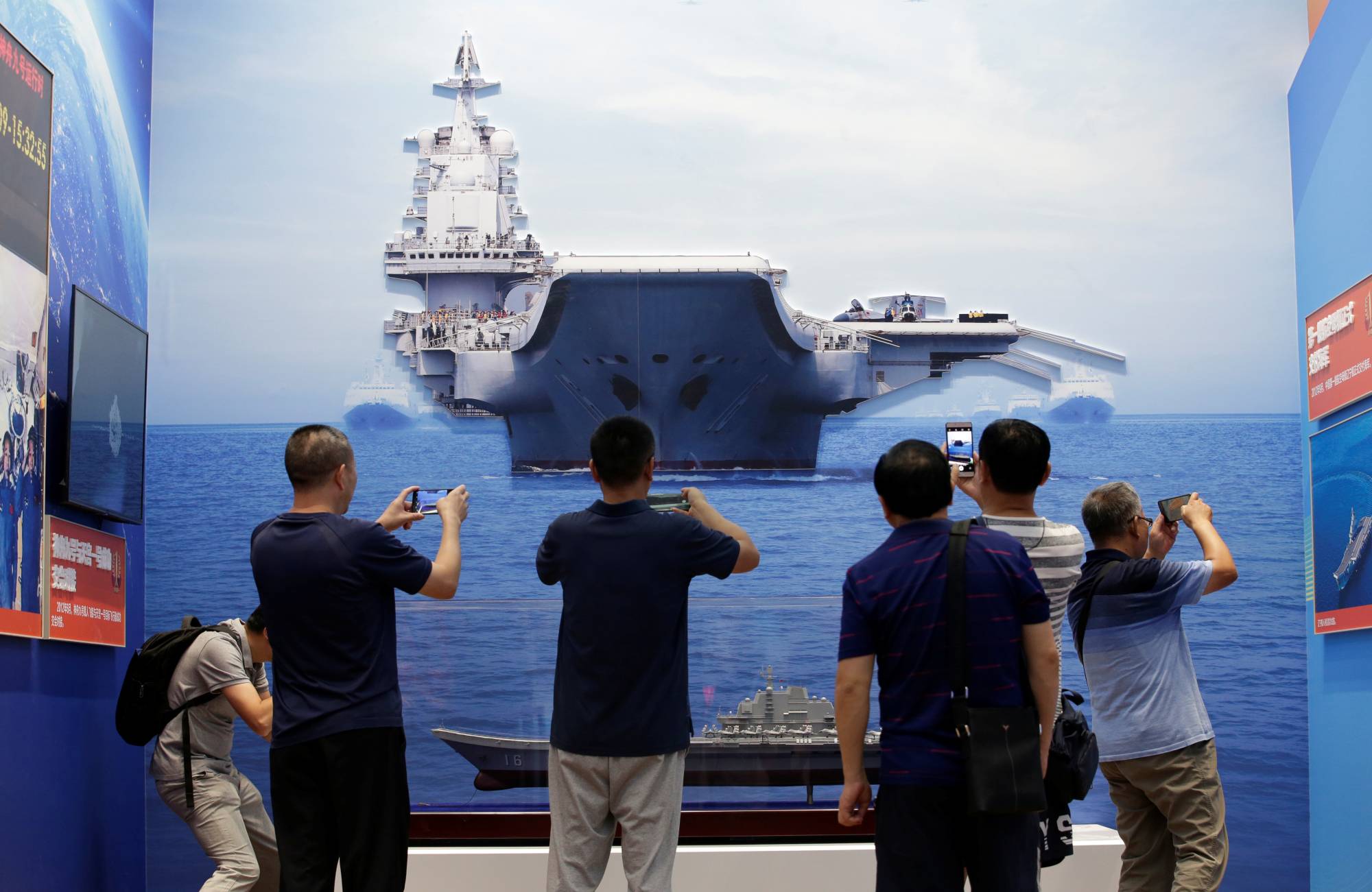 Visitors take photos of exhibits showing the Chinese People's Liberation Army Navy's first aircraft carrier, the Liaoning, during an exhibition at the Beijing Exhibition Center in the Chinese capital in September, 2019. | REUTERS