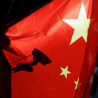A surveillance camera is silhouetted behind a Chinese national flag in Beijing. | REUTERS