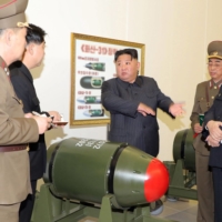 North Korean leader Kim Jong Un inspects a nuclear weapons project as a new, smaller nuclear warhead sits in front of him at an undisclosed location in the country, in this image released Tuesday. In the background, a poster appears to show how the green warheads can be mounted on a variety of missiles. | KCNA / KNS / VIA AFP-JIJI