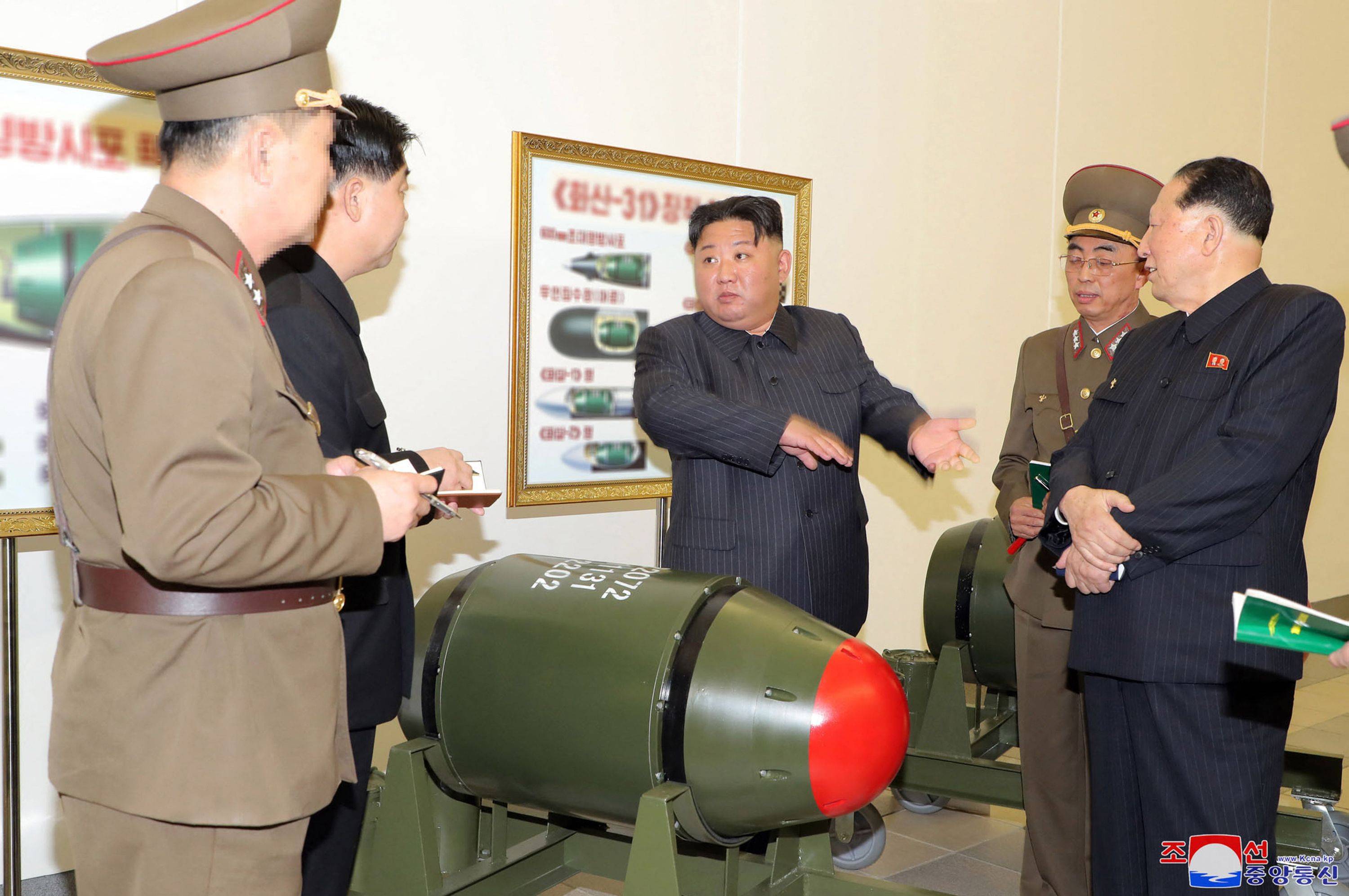 North Korean leader Kim Jong Un inspects a nuclear weapons project as a new, smaller nuclear warhead sits in front of him at an undisclosed location in the country, in this image released Tuesday. In the background, a poster appears to show how the green warheads can be mounted on a variety of missiles. | KCNA / KNS / VIA AFP-JIJI