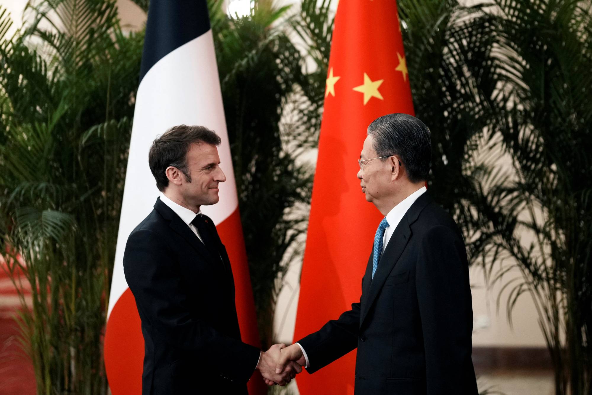 French President Emmanuel Macron (left) greets Zhao Leji, head of the National People's Congress, at the Great Hall of the People, in Beijing, on Thursday. | POOL / VIA REUTERS