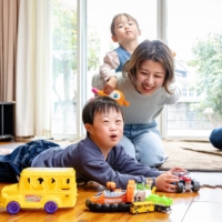 Takashi (right) and Chie Iwasaki smile at their son, Shoji (left), as their daughter, Ichika, rides on Chie’s back at their home in the city of Fukuyama, in Hiroshima Prefecture. | CHUGOKU SHIMBUN
