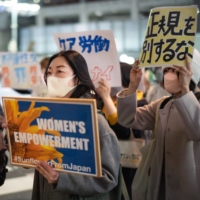 Demonstrators hold up signs during the Women\'s Day march in Tokyo in March. Japan\'s average female monthly income was ¥83,896 per month in February, far less than the average ¥345,645 salary for male workers. | BLOOMBERG