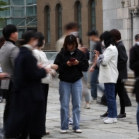Office workers look at their mobile phones to check the local online banking app Toss as they gather at the Seoul Museum of Art during a lunch break in Seoul on April 13.   | REUTERS