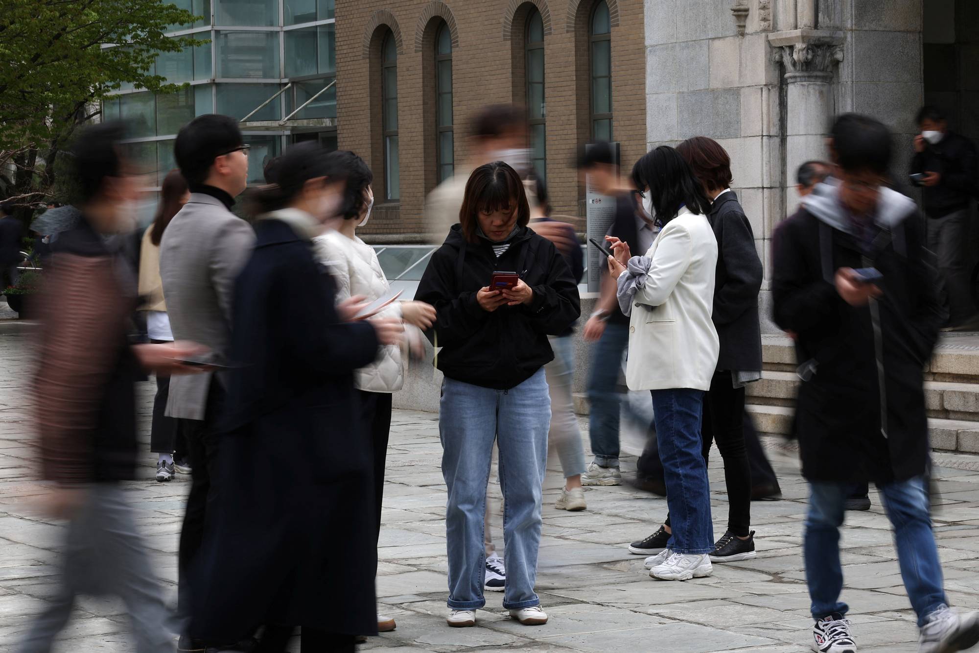 Office workers look at their mobile phones to check the local online banking app Toss as they gather at the Seoul Museum of Art during a lunch break in Seoul on April 13.   | REUTERS