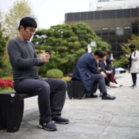 Kim Youngsuck, an office worker, looks at his mobile phone to check the local online banking app Toss at the Seoul Museum of Art during his lunch break in Seoul on April 13. | REUTERS