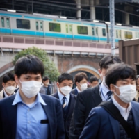 Morning commuters in front of Shimbashi Station in Tokyo on March 30. Over 60% of people in Japan surveyed in mid-March said they constantly keep face masks on when going out. | BLOOMBERG