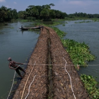 A man holds a rope as people transport floating beds toward a farm through the Belua river in Pirojpur district, Bangladesh, in August 2022.  | REUTERS
