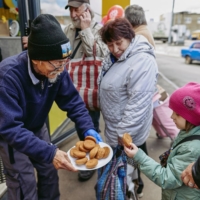 Fuminori Tsuchiko, a 75-year-old humanitarian volunteer from Japan, treats a girl with cookies outside of his cafe in Kharkiv, Ukraine, on Monday. | REUTERS