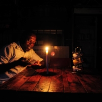 A restaurant owner counts cash by candlelight during a load shedding power outage in Johannesburg | BLOOMBERG