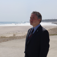 The Fukushima No. 1 Nuclear Power Plant is visible in the far background as William McMichael stands on a beach in Namie, which was devastated by tsunami following the 2011 Great East Japan Earthquake.