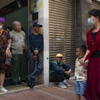 Mainland Chinese tourists wait for a bus outside an eatery in the To Kwa Wan neighborhood of Hong Kong. | ANTHONY KWAN / THE NEW YORK TIMES