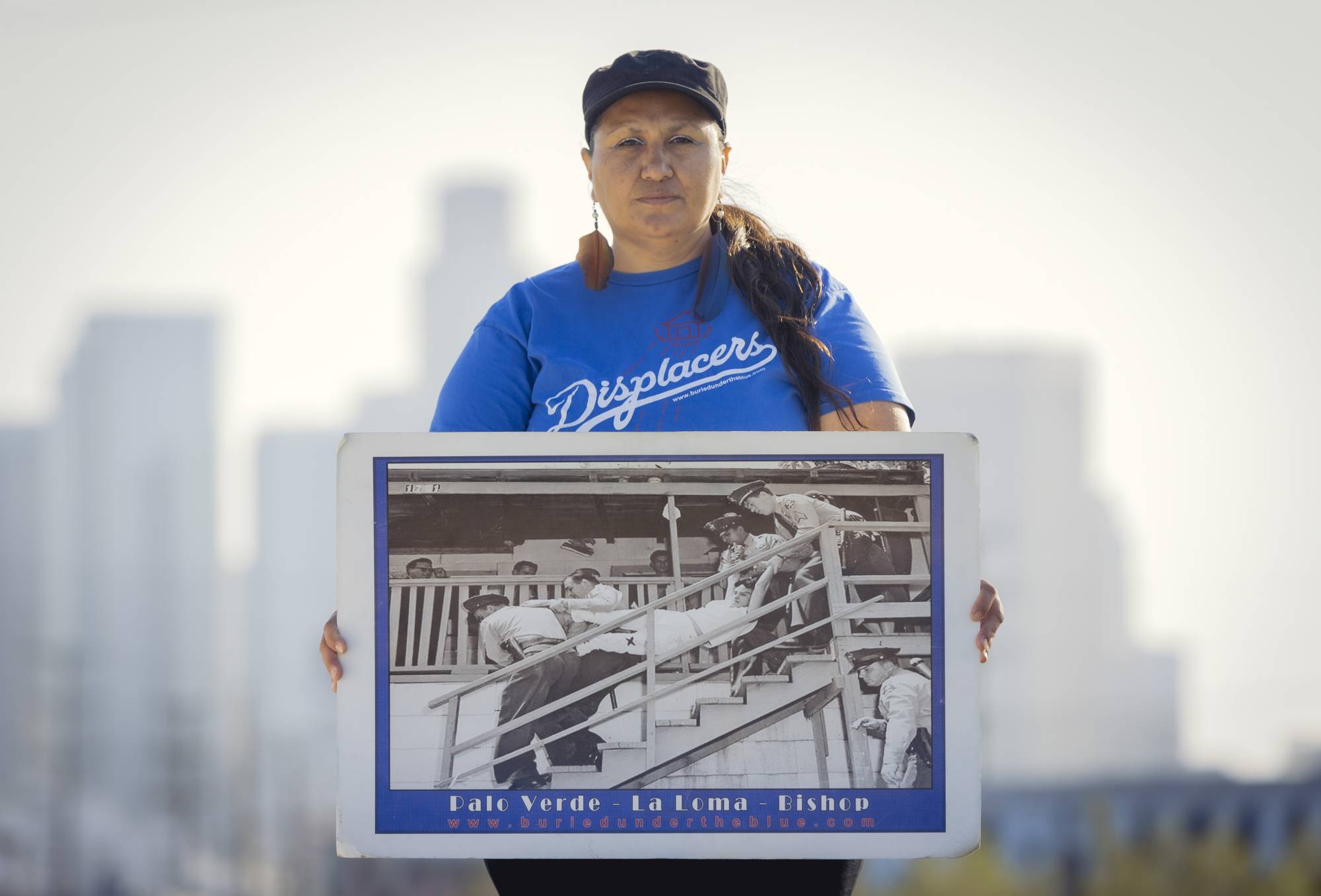 Melissa Arechiga holding a photo of her relative, Aurora Vargas, being carried out of her home in 1959, in Los Angeles on April 15. Dodger Stadium is the home to the seven-time world champion Los Angeles Dodgers. But in the 1950s, the land around it belonged to families who are now seeking reparations for what they lost. | CARLOS GONZALEZ / THE NEW YORK TIMES