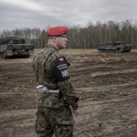 A member of the Polish military police stands watch as Leopard 2 tanks operated by Ukrainian soldiers take part in a demonstration at a military base in Swietoszow, Poland, in February. | MACIEK NABRDALIK / THE NEW YORK TIMES
