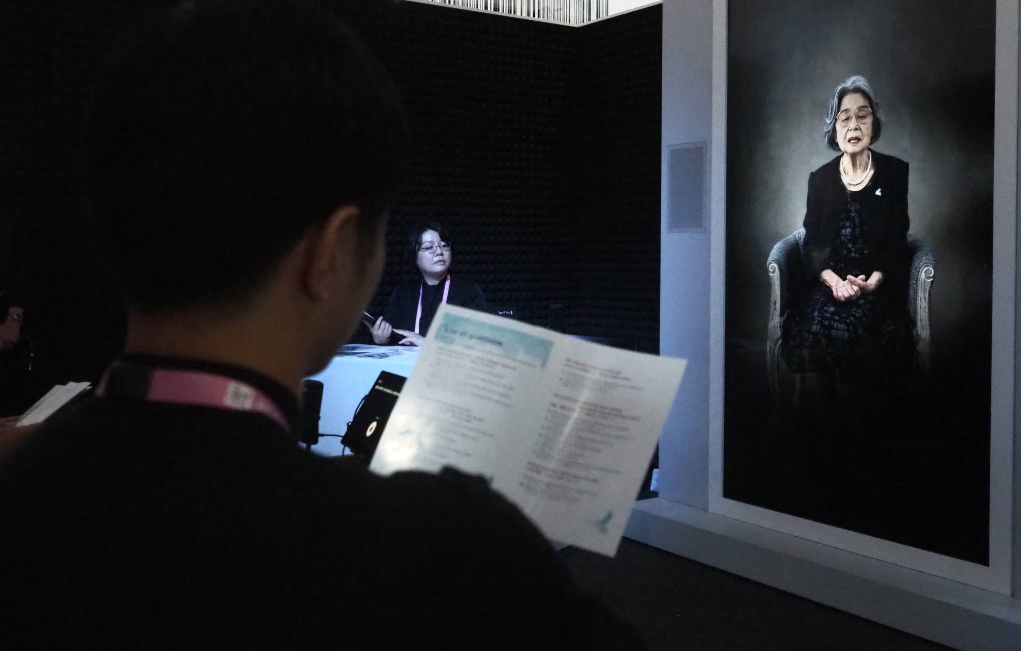A participant asks a question as a life-size video image of hibakusha Yoshiko Kajimoto is displayed at the media center on Friday.  | Daniel Traylor   
