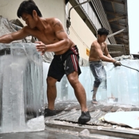 Workers move blocks of ice into a storage unit during a heat wave in Bangkok last month.  | AFP-JIJI