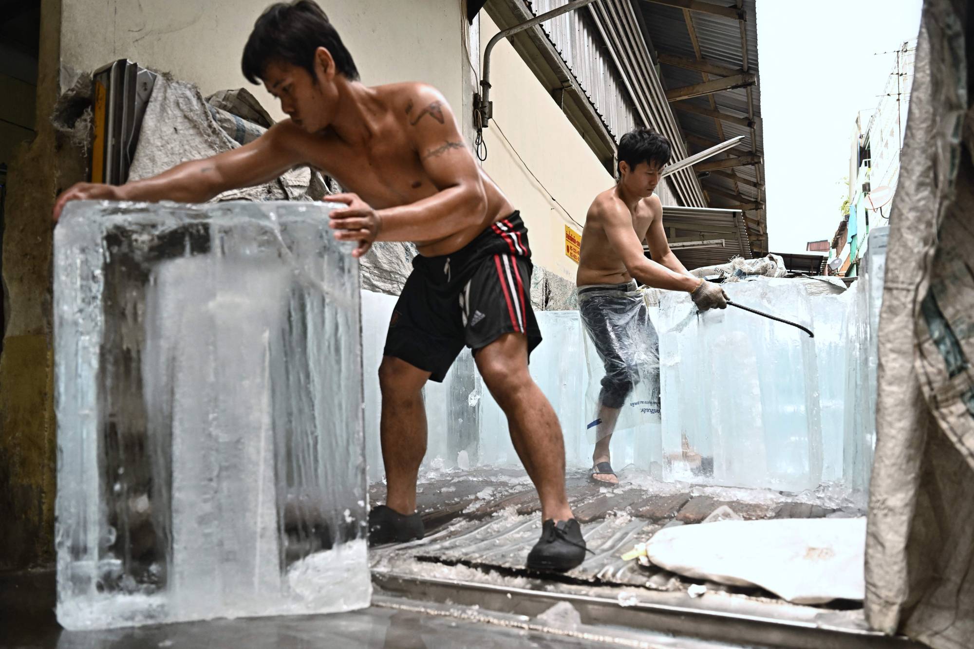 Workers move blocks of ice into a storage unit during a heat wave in Bangkok last month.  | AFP-JIJI