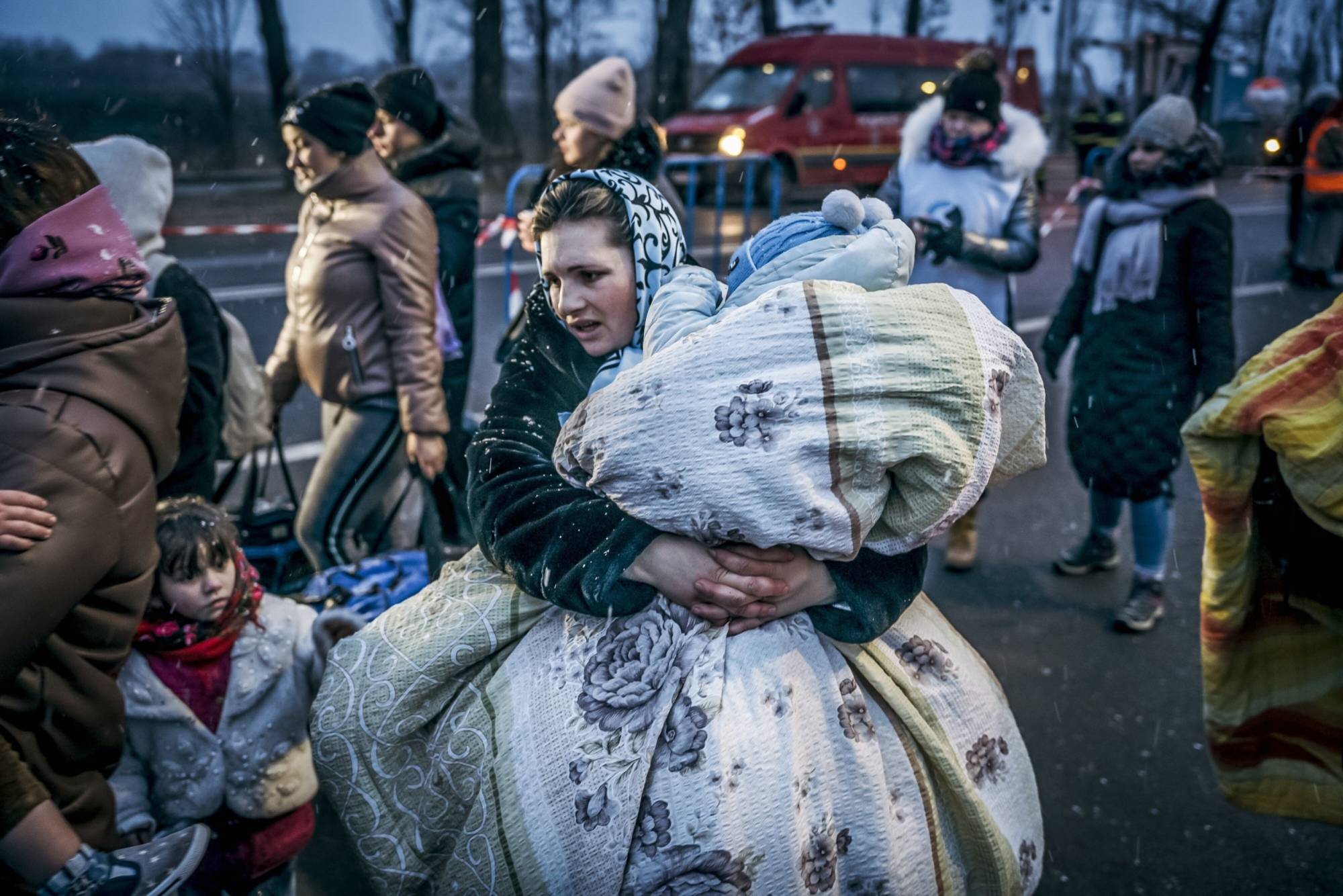 A displaced Ukrainian carries a child in a blanket after crossing the border in Siret, Romania, on March 2, 2022.  | BLOOMBERG