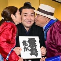 Mongolian-born sumo wrestler Kiribayama, who has changed his ring name to Kirishima, is kissed by his parents in Tokyo on Wednesday as he is promoted to the second-highest rank of ozeki. | POOL / VIA KYODO