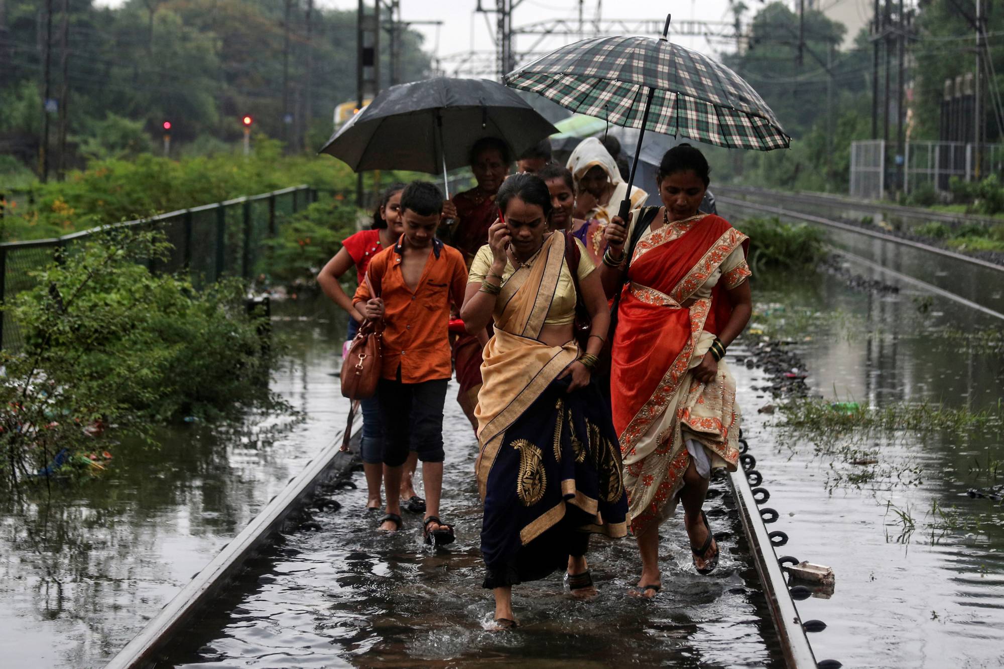 Commuters walk on waterlogged railway tracks after getting off a stalled train during heavy monsoon rains in Mumbai in July 2019.  | REUTERS