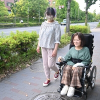 Yuda talks with a caregiver as she makes her way to a convenience store in Kyoto. Yuda says she wants to live the same way as able-bodied people. | NISHINIPPON SHIMBUN