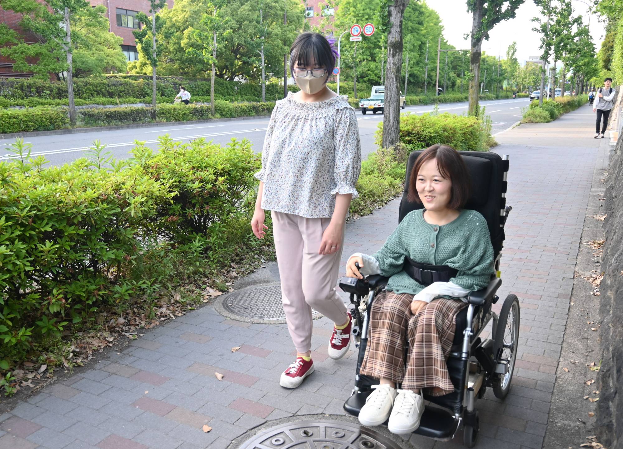 Yuda talks with a caregiver as she makes her way to a convenience store in Kyoto. Yuda says she wants to live the same way as able-bodied people. | Nishinippon Shimbun