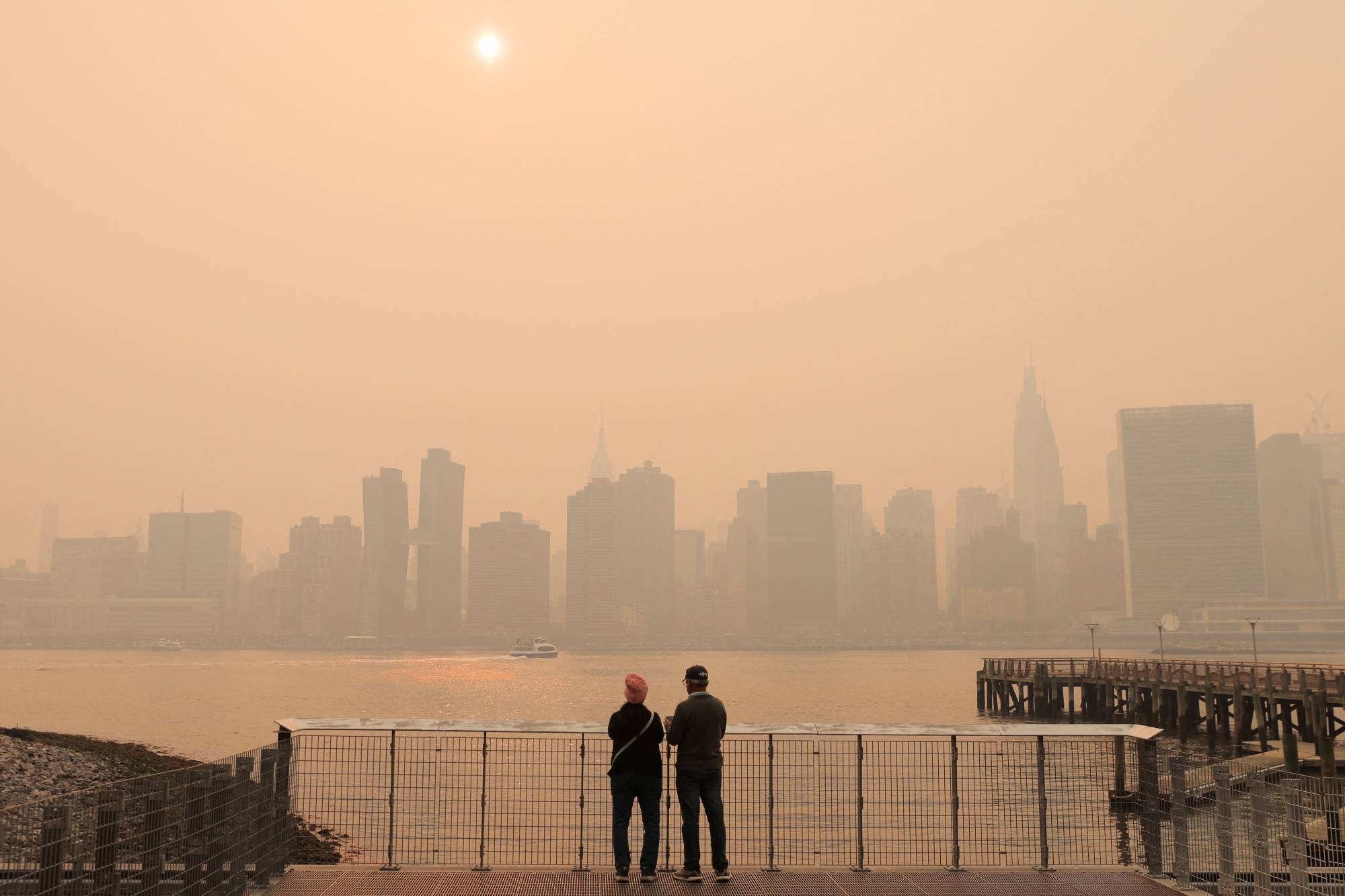 People watch the sunset as haze and smoke caused by wildfires in Canada hang over the Manhattan skyline, in New York on Wednesday. | REUTERS