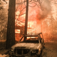 A structure burns behind a charred vehicle during the Oak Fire in Mariposa County, California, in July 2022. | BLOOMBERG