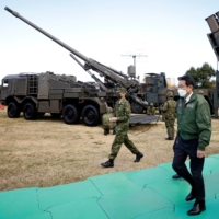 Prime Minister Fumio Kishida walks past a Ground Self-Defense Force Type-19 155 mm wheeled self-propelled howitzer and a Type-12 surface-to-ship missile as he inspects equipment during a review at the SDF\'s Camp Asaka in Tokyo in November 2021. | POOL / VIA REUTERS