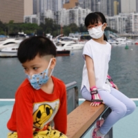 Children wearing face masks rest next to Victoria Harbour, in Hong Kong, in March 2022.  | REUTERS