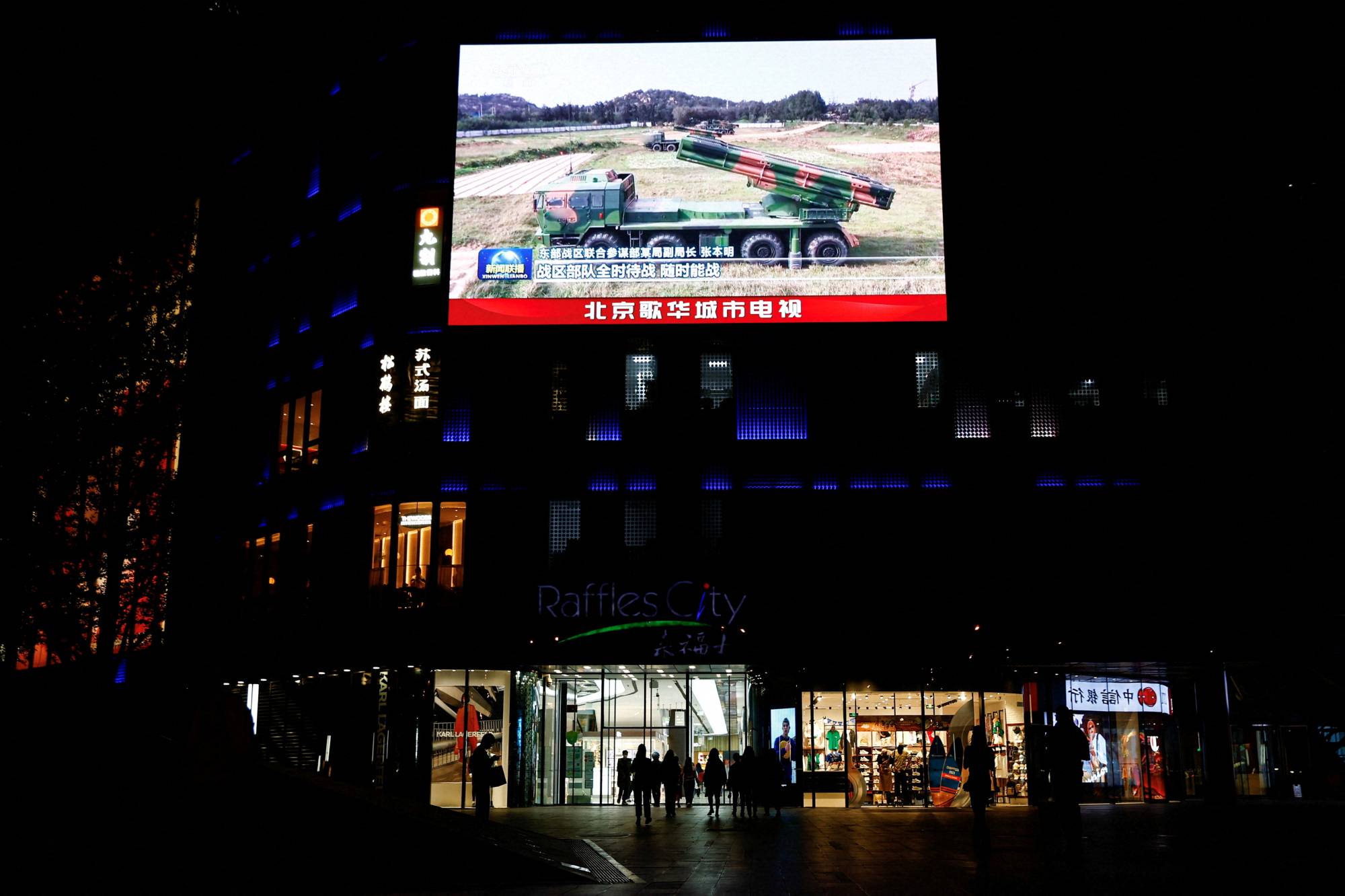 A giant screen displays news footage of military vehicles under the Eastern Theatre Command of China's People's Liberation Army taking part in joint military exercises around Taiwan, at a shopping mall in Beijing on April 10. | REUTERS