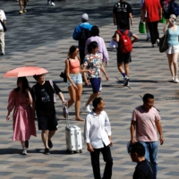 People walk through a shopping area amid a heat wave in Beijing on Thursday. Temperatures in parts of Asia have risen above 40 degrees Celsius in recent months, causing widespread infrastructure damage and power outages. | REUTERS
