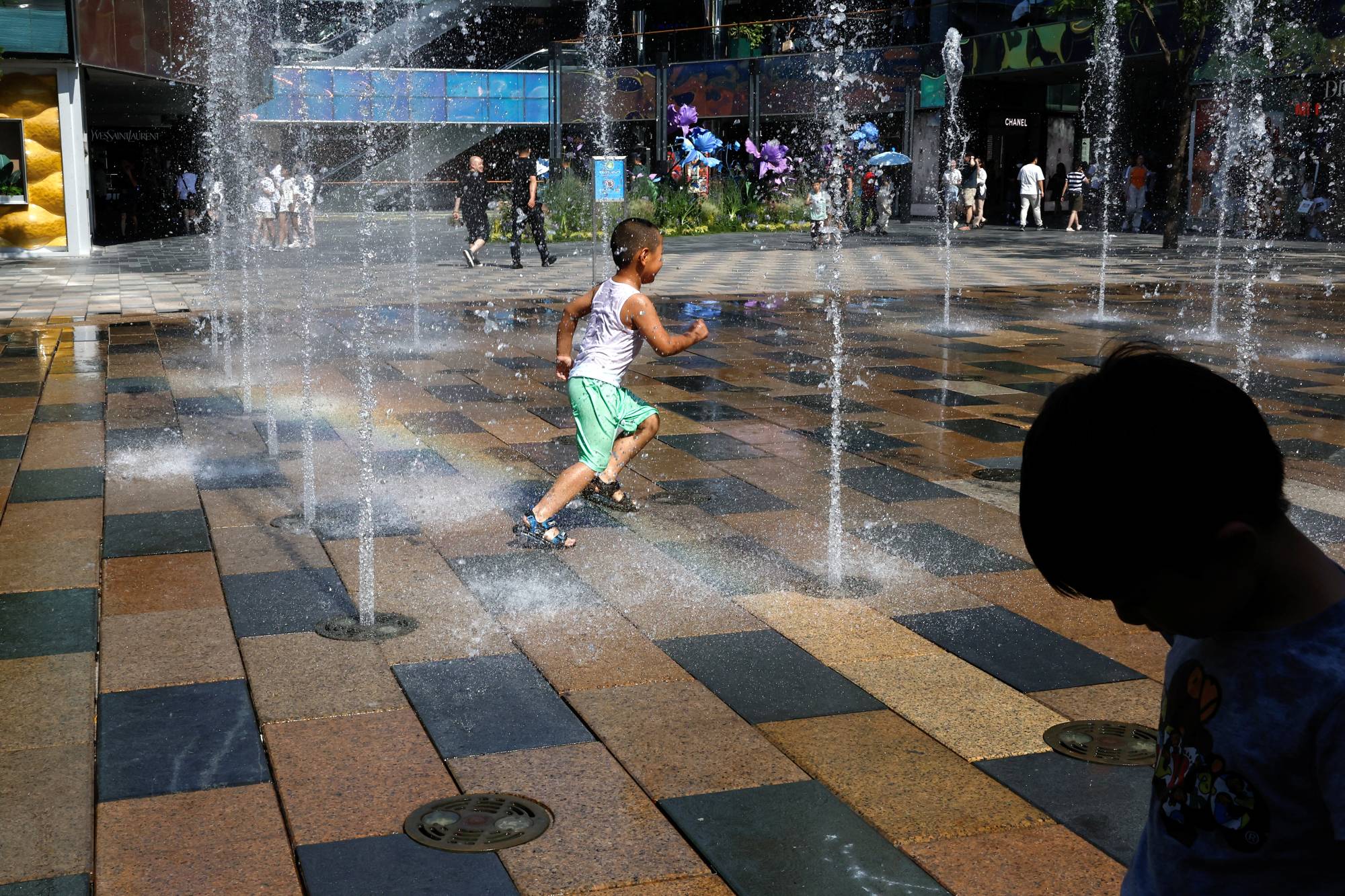 Children cool off in a water fountain amid a heat wave, at a shopping area in Beijing on Thursday. | REUTERS