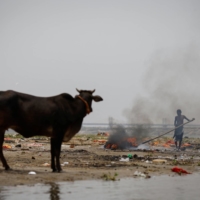 A man adjusts a burning pyre at a cremation ground on the banks of Ganges River in the northern state of Uttar Pradesh, India, on Wednesday. | REUTERS