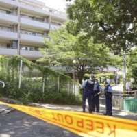 Police officers stand guard at a condominium where an 18-year-old woman was found stabbed Thursday. She was later pronounced dead. | KYODO