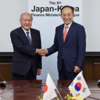 Finance Minister Shunichi Suzuki (left) and his South Korean counterpart Choo Kyung-ho shake hands at a meeting in Tokyo on Thursday. | JAPAN\'S FINANCE MINISTRY / VIA AFP-JIJI