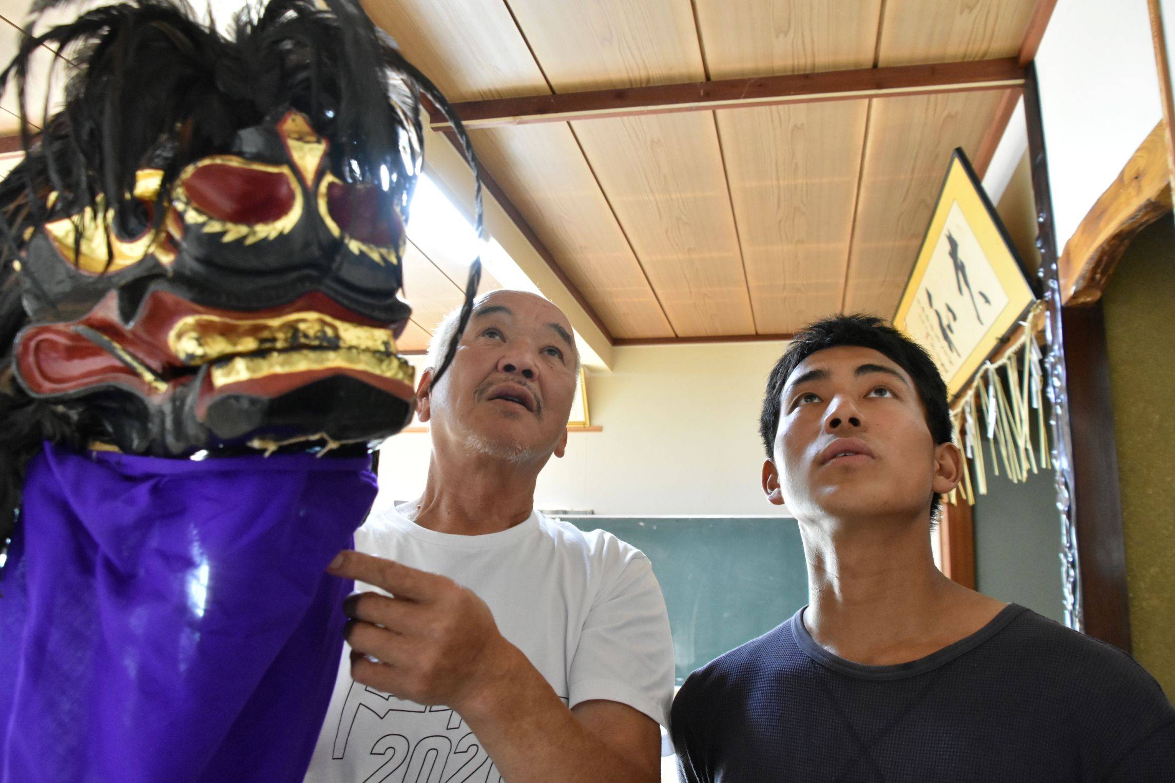 Kenichi Koike (left), head of a preservation group for Saikatsu no Higan-jishi, a traditional folk dance handed down in Fukushima Prefecture, explains its history to Takeo Oshima, a new member of the group, at a community center in Aizumisato in the prefecture. | FUKUSHIMA MINPO