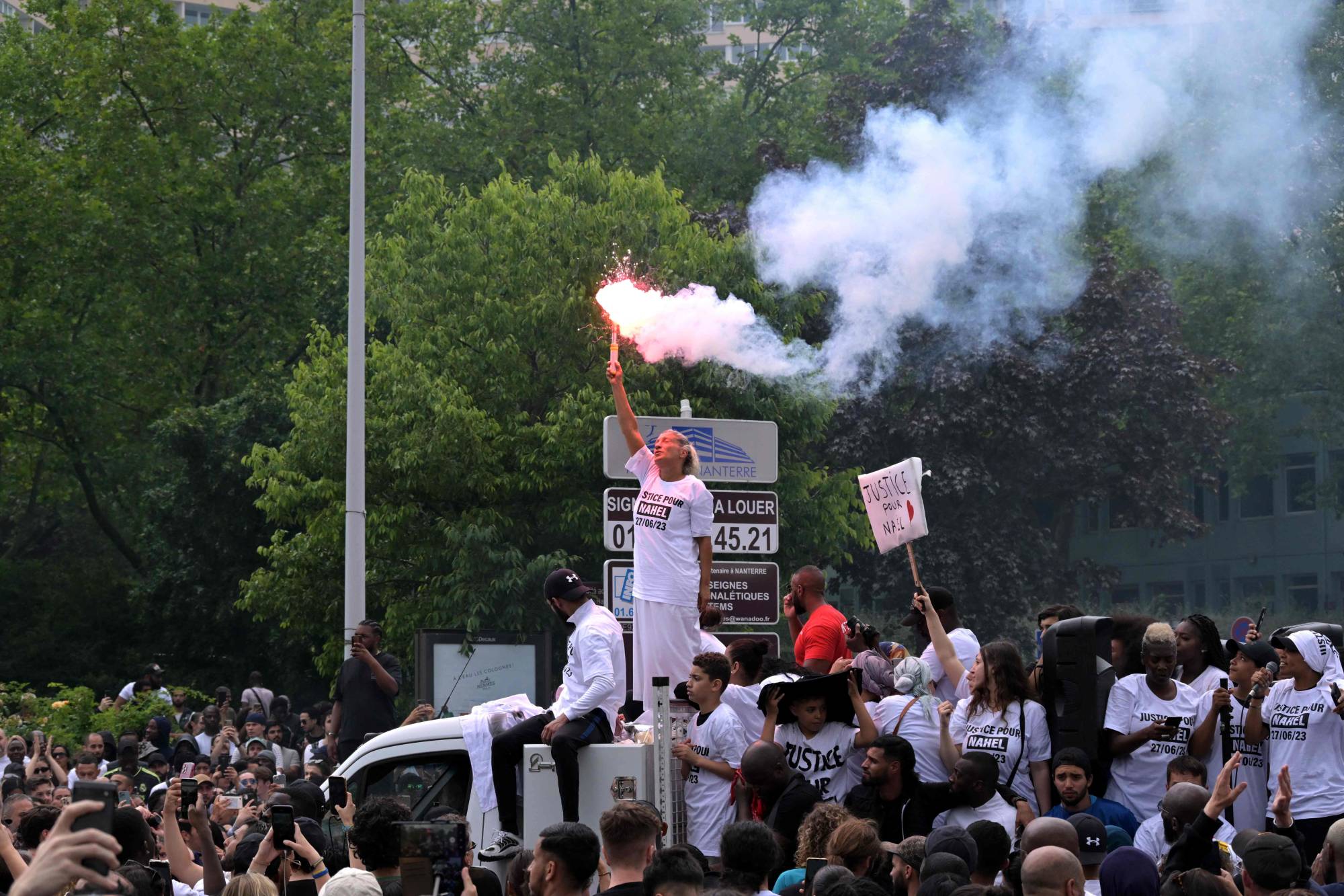 Mounia, the mother of Nahel, a teenage driver shot dead by a policeman, waves a light flare as she stands atop a truck during a commemoration march for her son, in the Parisian suburb of Nanterre, on Thursday.  | AFP-JIJI