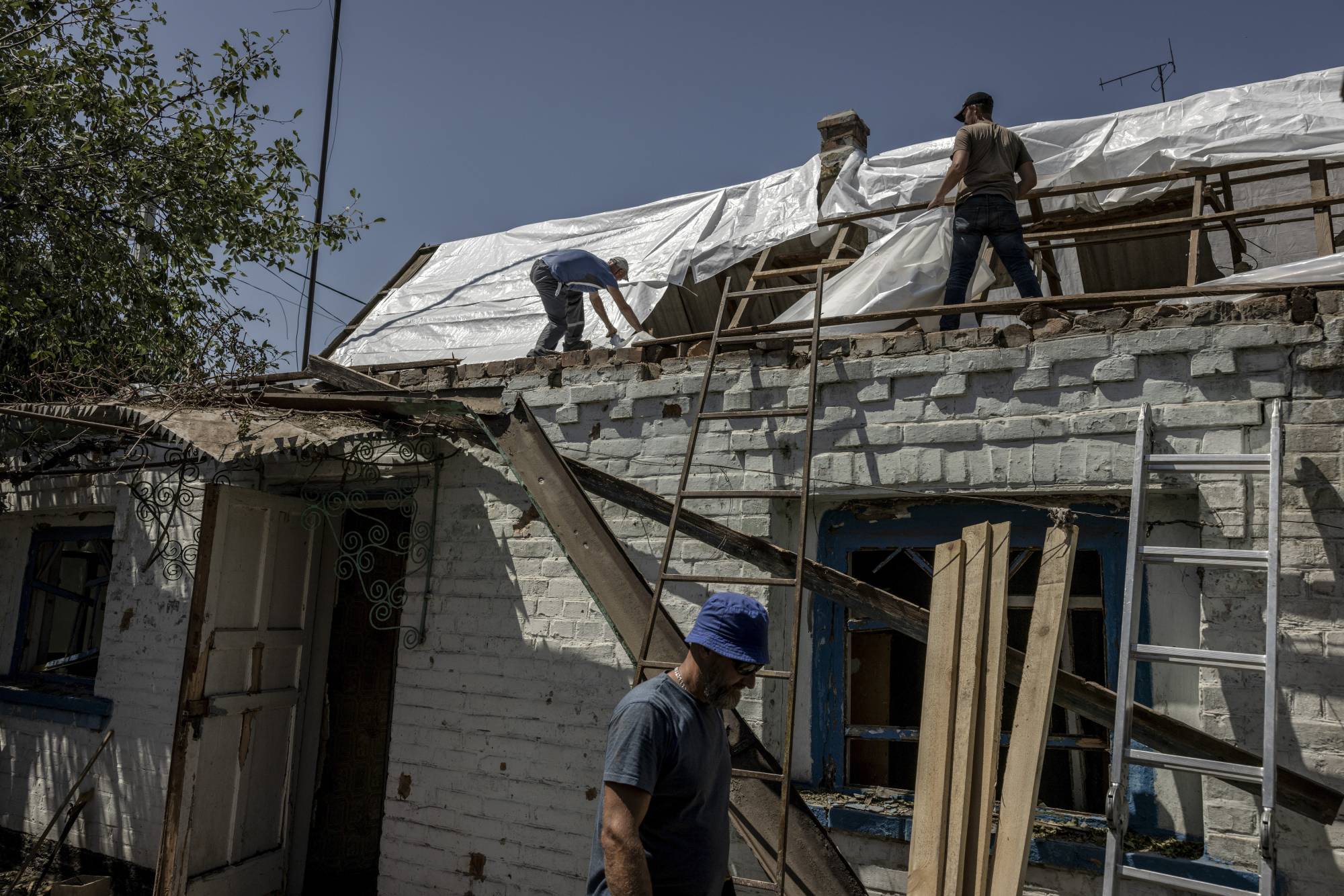 Residents repair a home damaged overnight by Russian shelling in Nikopol, Ukraine, on July 3. Ukrainians who live near the Russian-Occupied Zaporizhzhia Nuclear Power Plant have grown largely complacent about the dangers despite urgent government warnings.  | FINBARR O’REILLY / THE NEW YORK TIMES