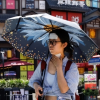 A woman with cold patches on her neck and forehead tries to beat the heat in Beijing. | REUTERS