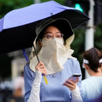A woman shields herself from the sun as she walks on a street, using a hat, mask and umbrella, amid a heat wave alert in Shanghai on Tuesday. | REUTERS