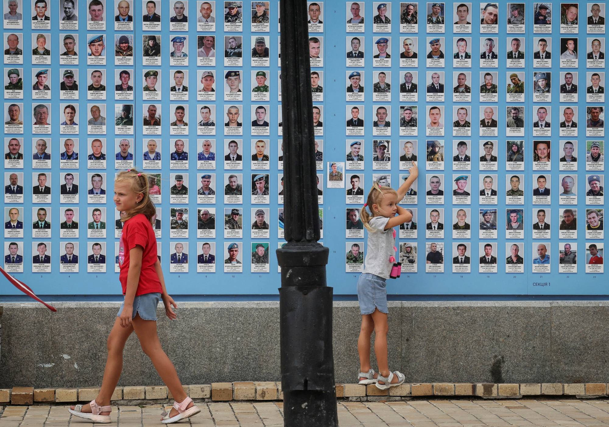 Girls play next to the memory wall of fallen defenders of Ukraine in Kyiv this month. | REUTERS