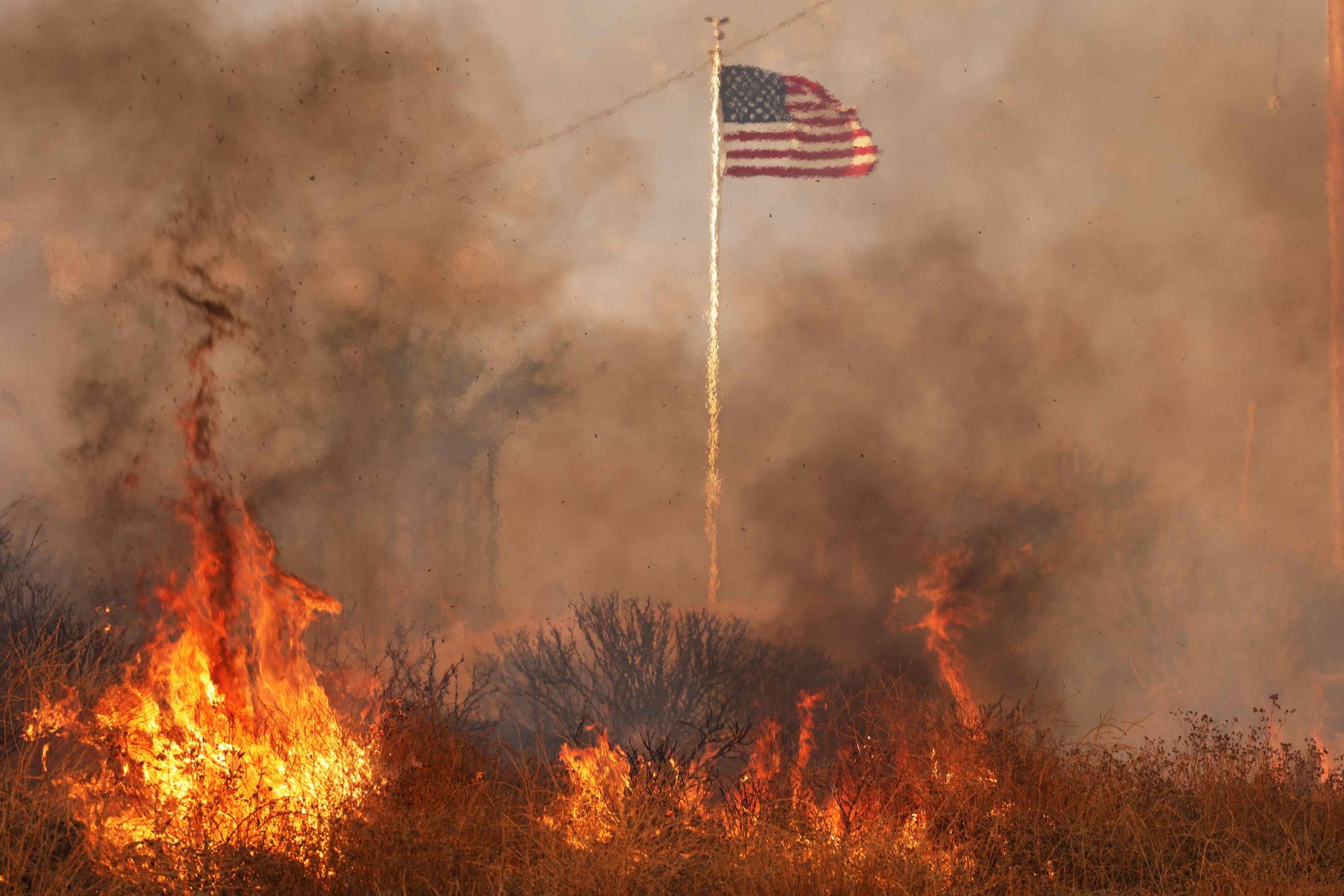 The United States national flag surrounded by flames during a fire in Moreno Valley in Riverside County, California, on Friday. | AFP-JIJI