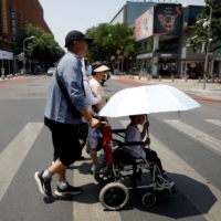 Pedestrians cross a road on a hot day amid an orange alert for heat wave, in Beijing, on Sunday. | REUTERS