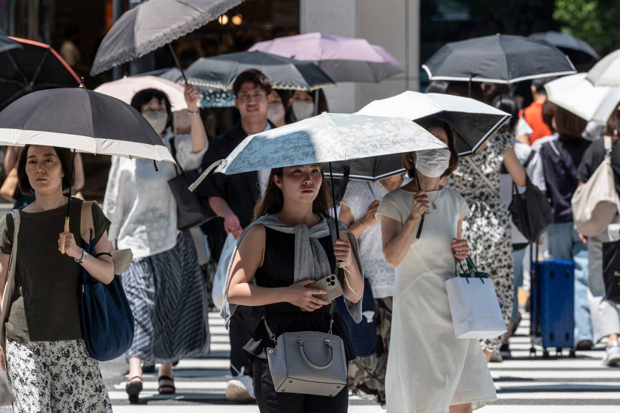 People with parasols cross the street in downtown Tokyo on Monday amid scorching heat. | AFP-JIJI