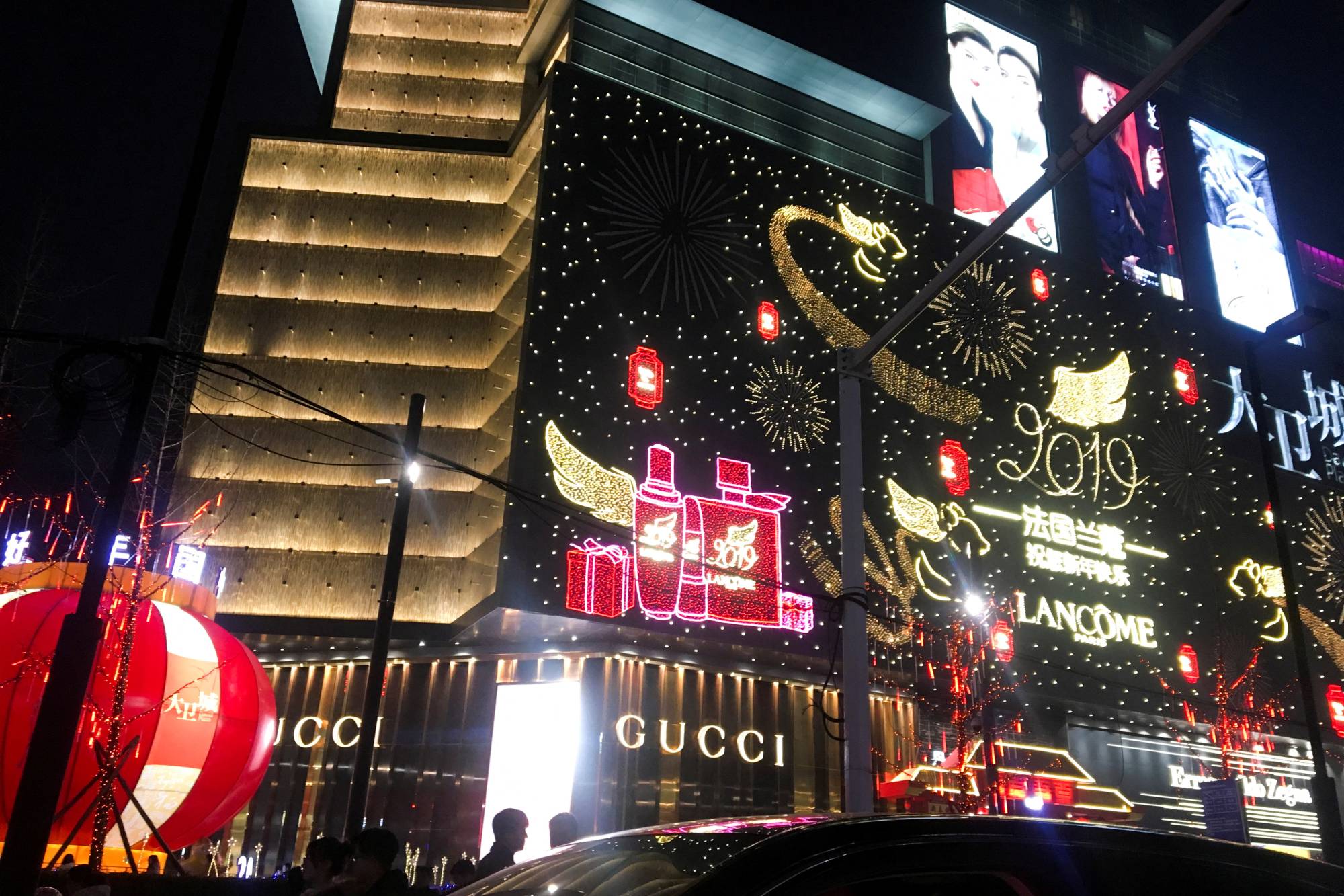 Neon signs in the shapes of luxury brand names illuminate the facade of David Plaza, a shopping mall in Zhengzhou, China, in 2019. | REUTERS