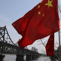 A Chinese national flag flutters near the Friendship Bridge and Broken Bridge over the Yalu River, which separates North Korea\'s Sinuiju from Dandong, China, in April 2021.  | REUTERS