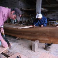 Douglas Brooks works with Ryujin Shimojo to build a sabani in December 2009 as the American boat builder chronicles the craft of building a traditional, wooden Okinawa fishing boat. Below: Brooks sits in front of Shimojo\'s workshop on Iejima Island, Okinawa Prefecture. | PHOTOS COURTESY OF DOUGLAS BROOKS, MICK CORLISS